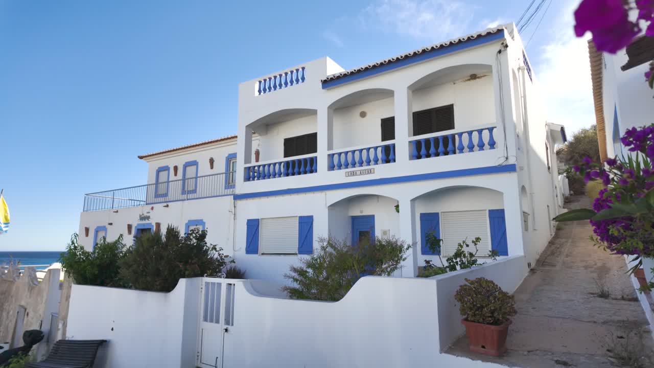 White and blue coastal villa with vibrant pink flowers in the foreground, showcasing the clear blue sky and sea, perfect for a serene vacation spot.