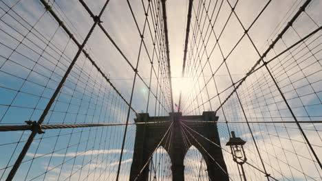 slider shot of the brooklyn bridge the sun high in the sky will light above the pillars of the bridg