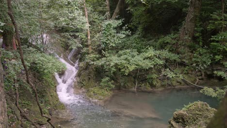 slow motion pan right to left, reveal waterfalling to blue water pond