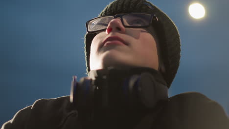 close-up of a young boy wearing glasses and a black jacket adjusts his glasses, looking thoughtful, he has a headset around his neck