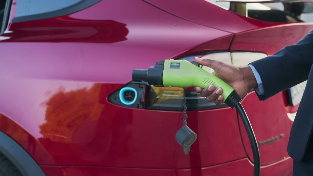 럭셔리 레드카를 위한 녹색 전기 충전 플러그를 들고 있는 남성의 가까운 손.