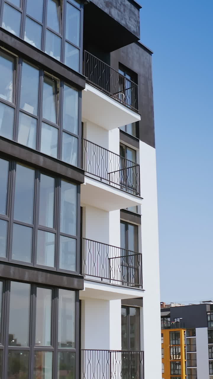 Modern multi-storey building. Large glazed balconies of the new high-rise building. Black and white apartment building in modern design in the city. Camera rising. Vertical video