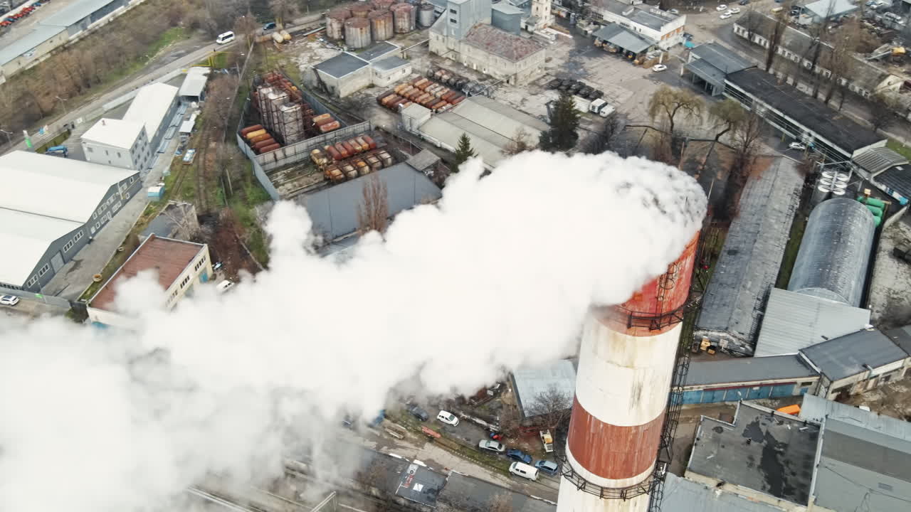 Aerial drone view of thermal station with smoke coming out of the tube. Buildings, roads and bare trees on the background. Cloudy weather. Chisinau, Moldova