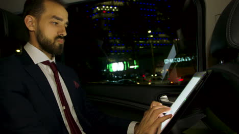 ceo in business suit working on tablet in the back of luxury car