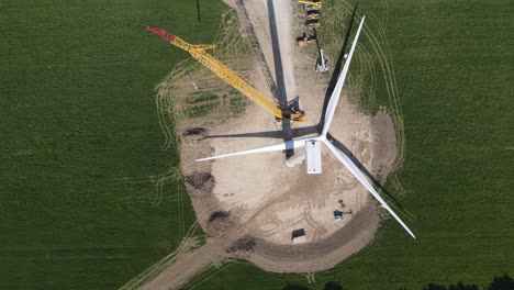 crane building wind turbine in green fields, top down view