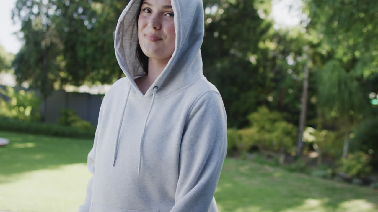 Happy caucasian woman in white hooded top in sunny garden in slow motion with copy space