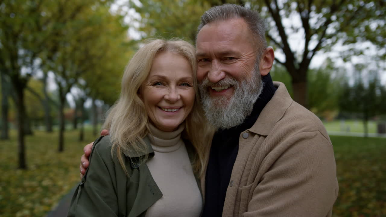 Portrait of happy senior lovers posing for camera with smiling faces in park.