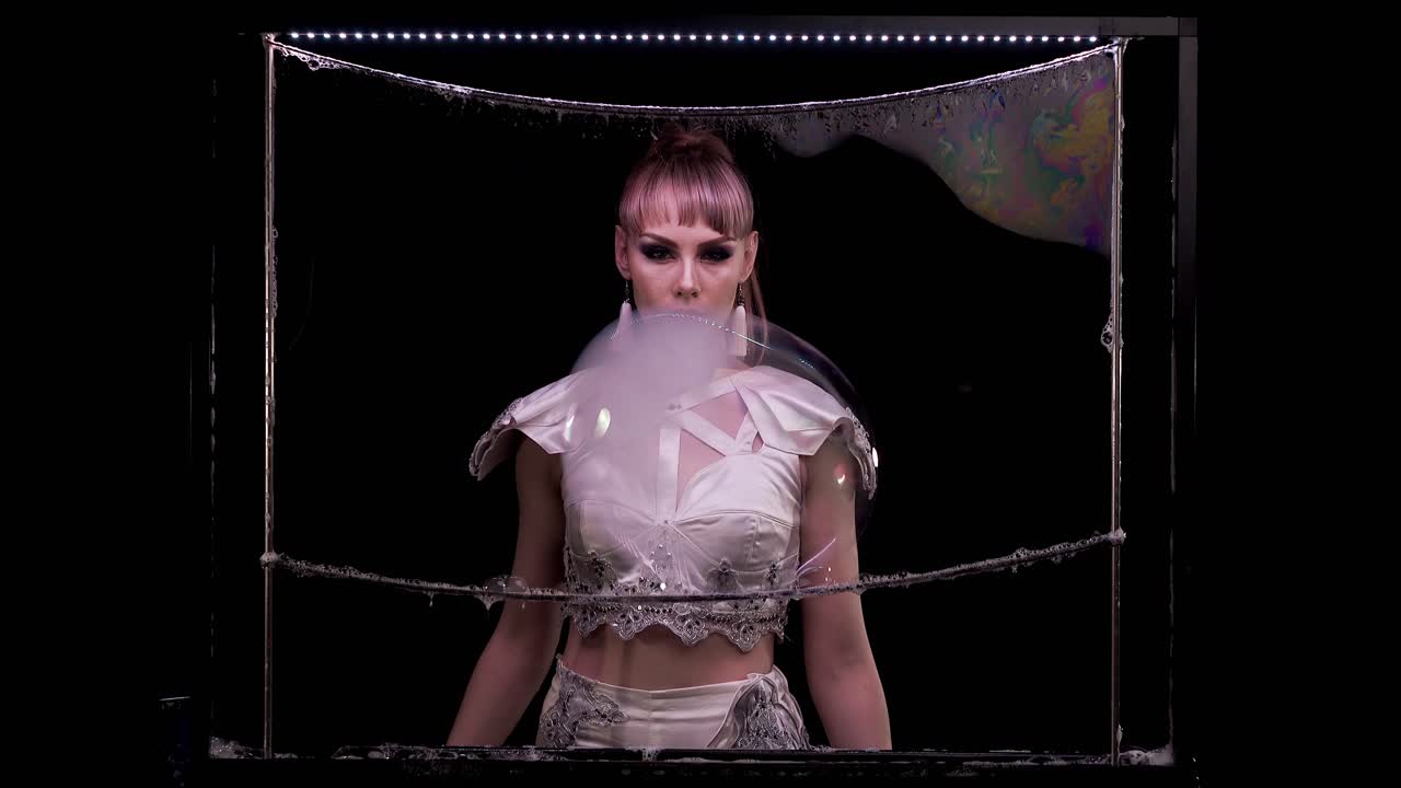 예쁜 소녀는 손가락을 사용하여 두 개의 큰 거품을 가지고 놀다가 연기로 하나에 연결합니다.