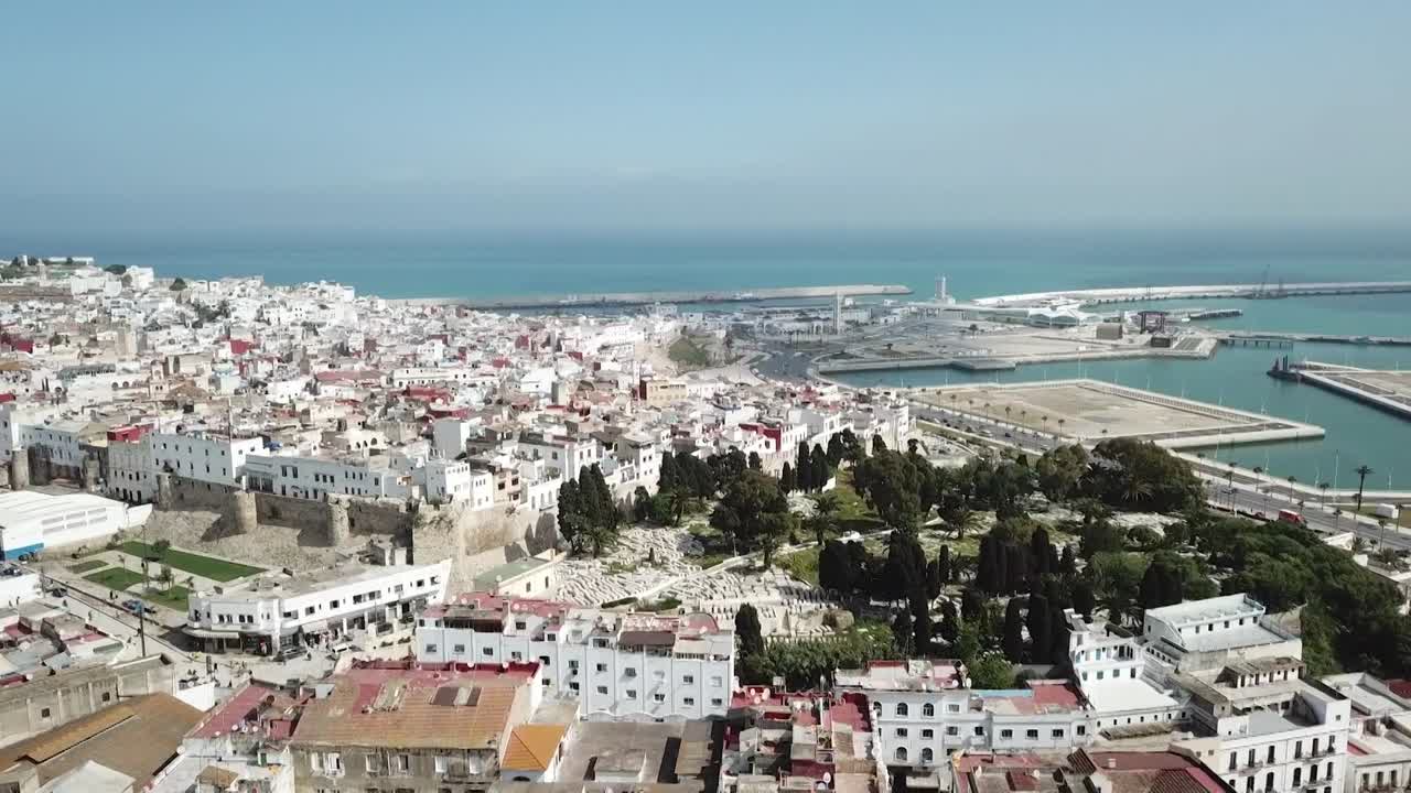 Ripresa panoramica con drone che mostra i tradizionali edifici bianchi di Tangeri. Con lussureggianti colline verdi, tetti storici e la moderna infrastruttura portuale sulla costa mediterranea