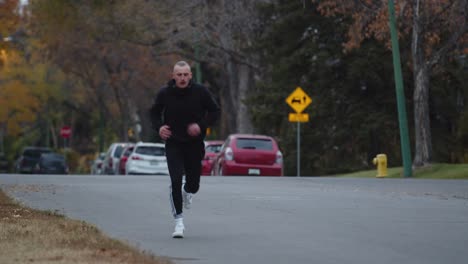 young man wearing a black tracksuit running in a neighborhood