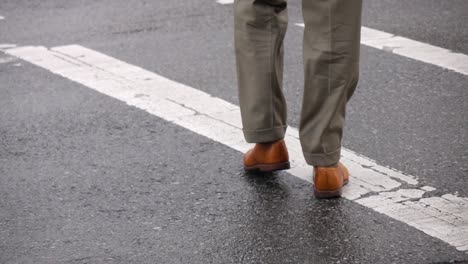 primer plano en ángulo bajo de un hombre vestido con pantalones y zapatos formales mientras cruza la calle