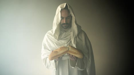 jesus christ in white hooded robe breaking bread in bright glowing light. perfect for easter visual, gospel symbolism of jesus as the bread of life.