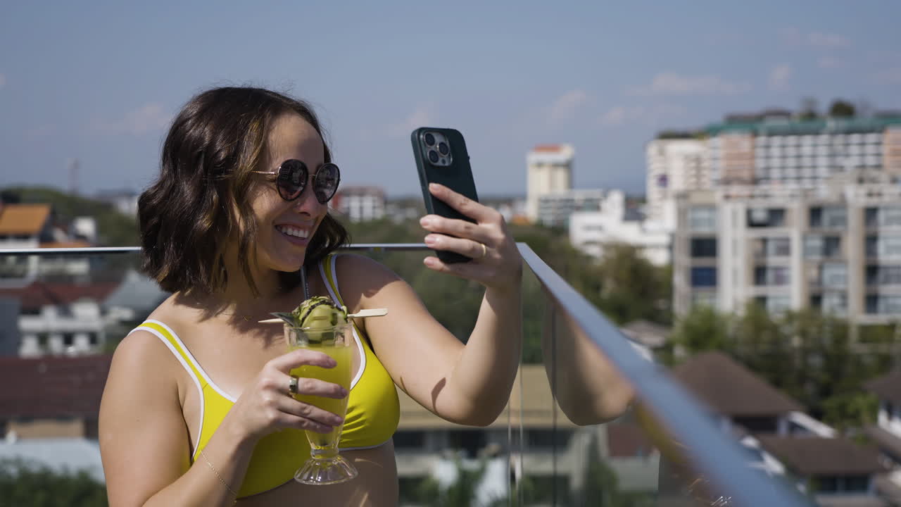 Cena em câmera lenta de uma mulher de biquíni bebendo um coquetel e tirando selfies