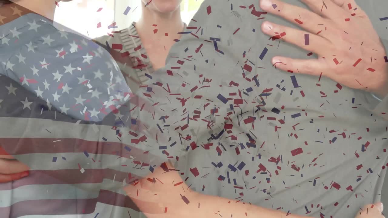 Confetti falling over waving american flag against businesspeople hugging each other at office