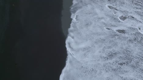 large white surf waves crashing onto the black sand