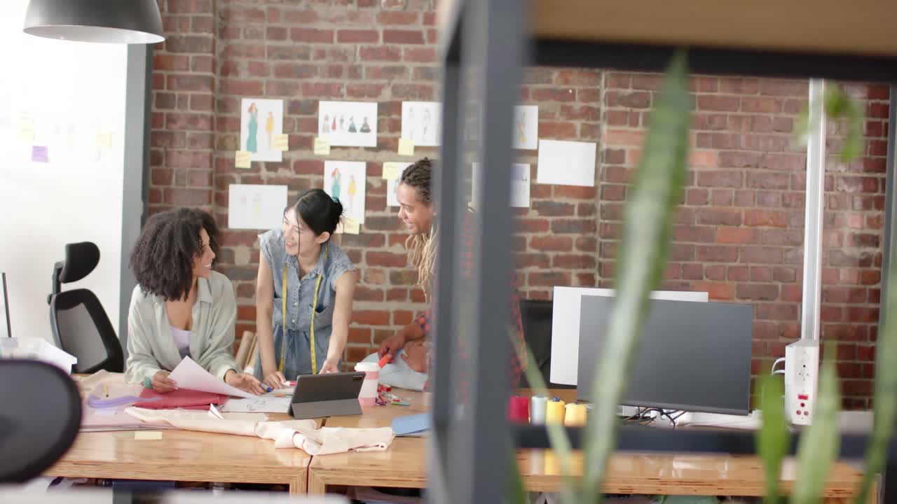 ラップトップを使用して忙しい多様なデザイナーが ⁇ スローモーションでファッションデザインスタジオでの作業について議論しています ⁇