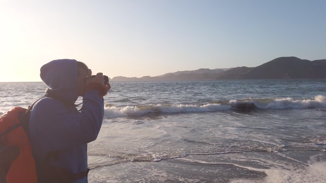 Young adult man taking pictures of sunlit seascape on Baker Beach San Francisco