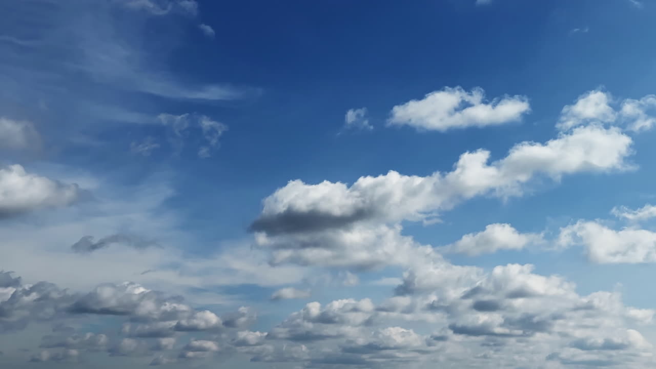 White small fluffy clouds transform in the blue sky. Cumulus clouds change shape in the atmosphere. Low angle view. Timelapse.