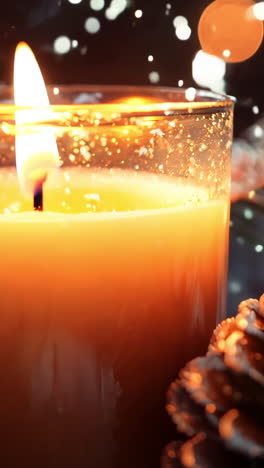 a candle is lit in a glass jar with pine cones on a table. the scene is warm and cozy, with the candle providing a soft glow that illuminates the pine cones