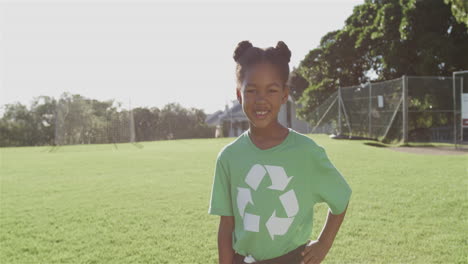 biracial girl stands proudly in a sunny outdoor park wearing a green recycling t-shirt