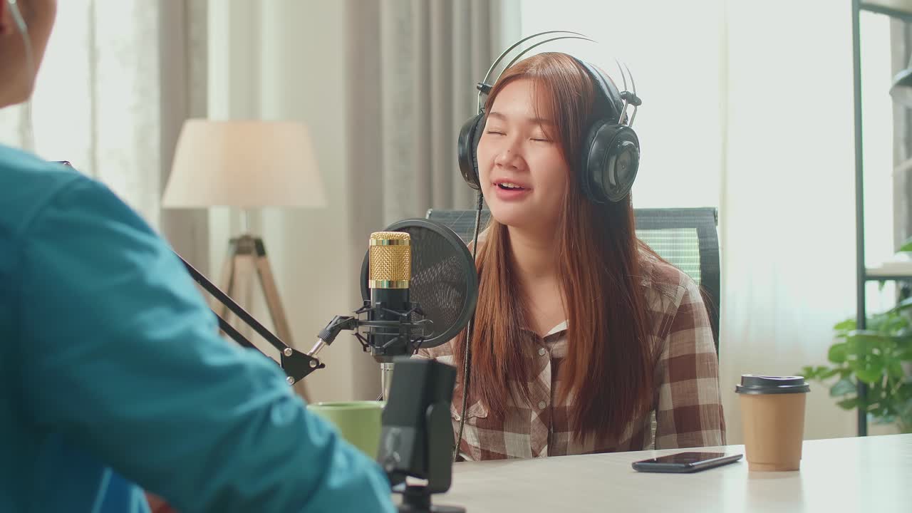 Over Shoulder View Of Asian Man Host Record Podcast Use Microphone Wear Headphone Interview Guest Conversation For Content In His Home Studio. Content Creator Concept