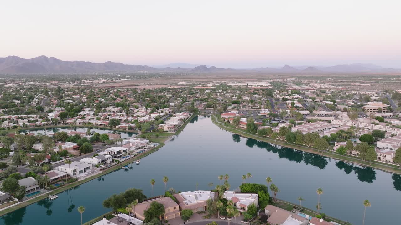 Scottsdale lake surrounded by houses, palm trees, and distant mountains at dusk , aerial view