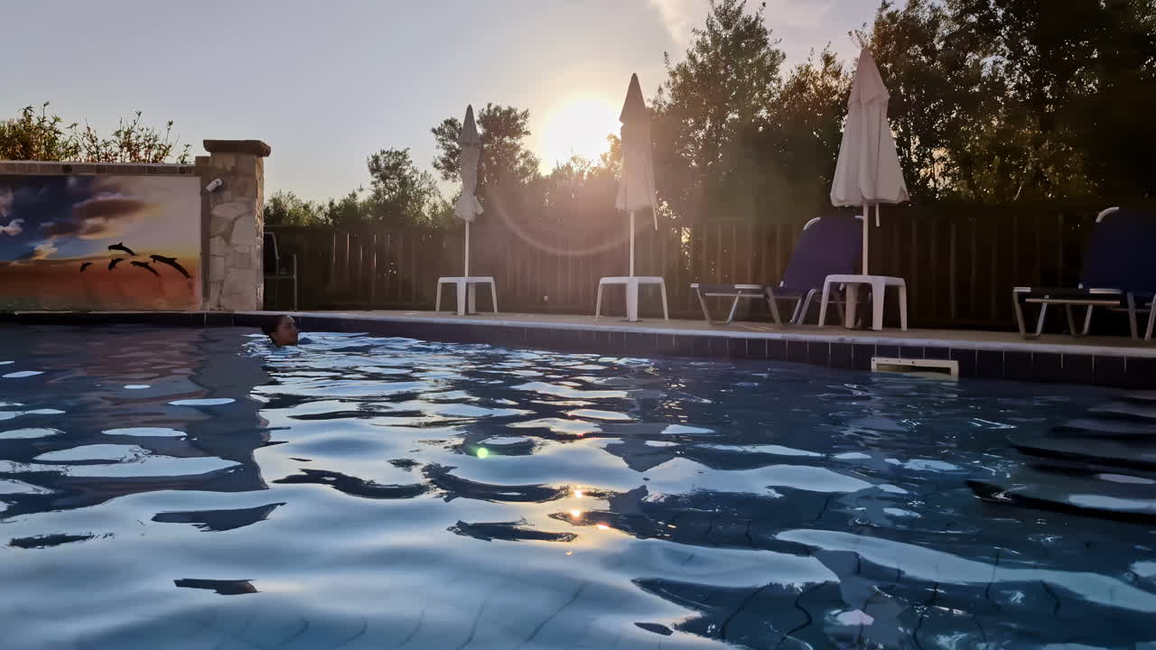 mujer morena nada en cámara lenta una piscina de hotel con árboles al atardecer de fondo