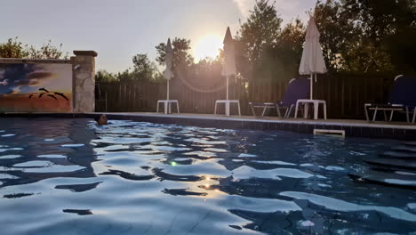 brunette woman swims in slow motion a hotel pool with sunset trees background