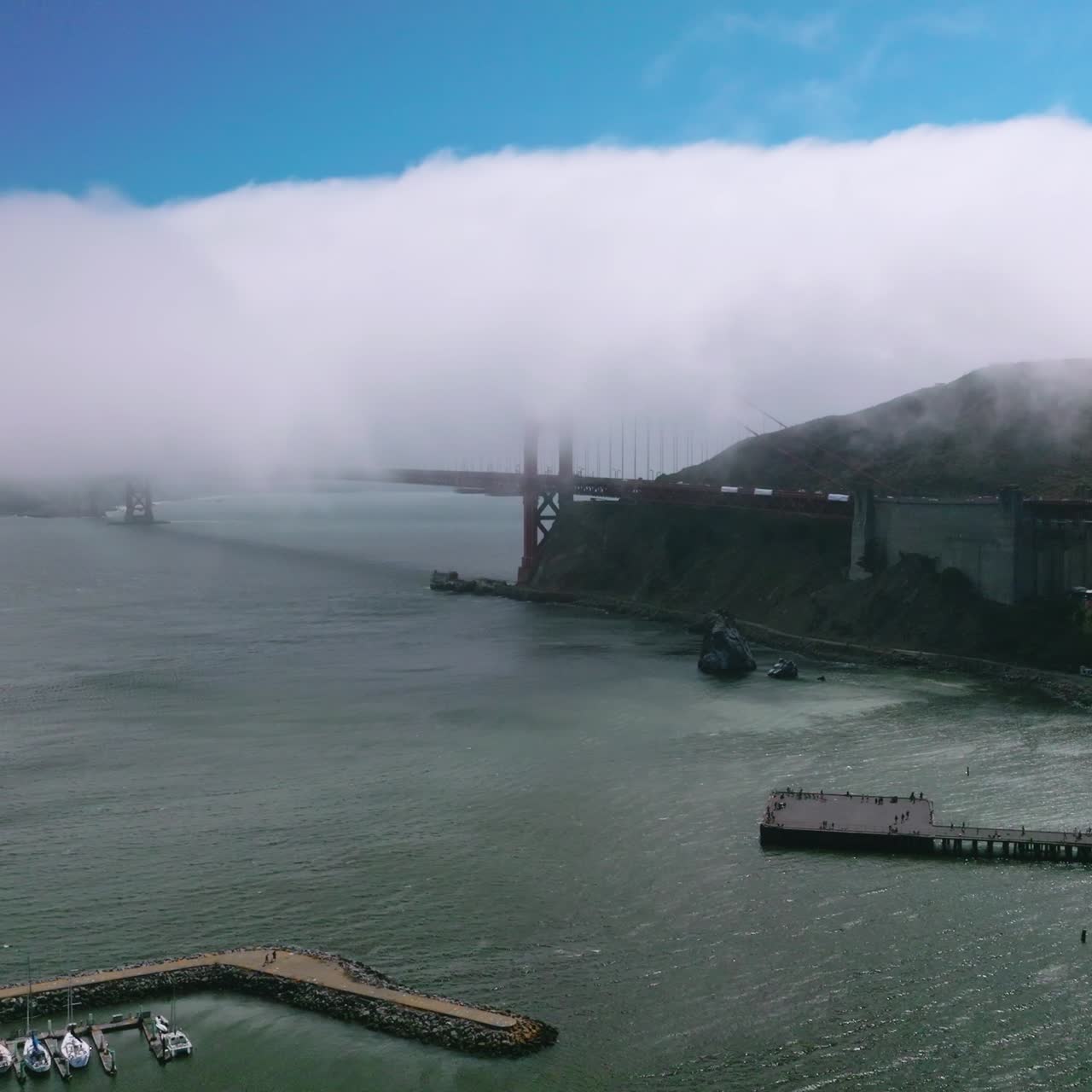 A huge wave of white thick fog hiding the famous San Francisco landmark. Beginning of the Golden Gate Bridge coated with haze