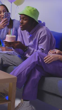 vertical video studio shot of gen z friends celebrating man's birthday with party cake and candles sitting on sofa