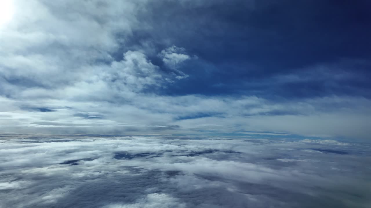 A pilot’s perspective from the cockpit of a plane flying between layers of ethereal clouds under a faded sun shining above in the left frame corner