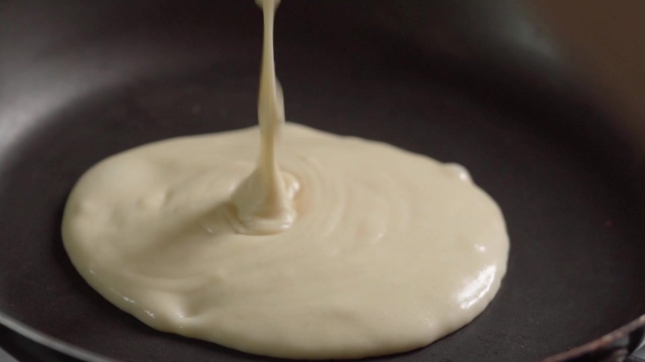 Primo piano che mostra la pastella per pancake versata su una padella calda e che forma una forma rotonda durante la cottura per la preparazione di una colazione fresca fatta in casa.