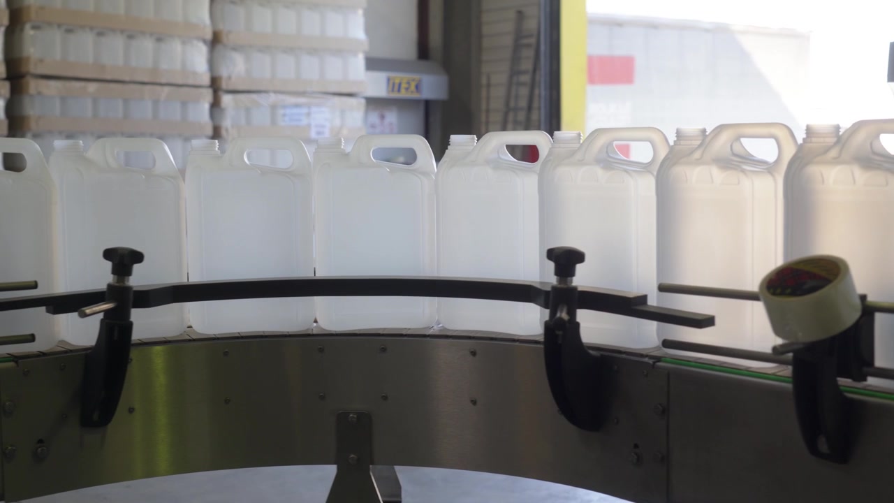 Weiße Plastikkanister bewegen sich auf einem industriellen Förderband in einer Fabrik. Automatisierte Produktionslinie und Lagerung in einer chemischen Abfüllanlage