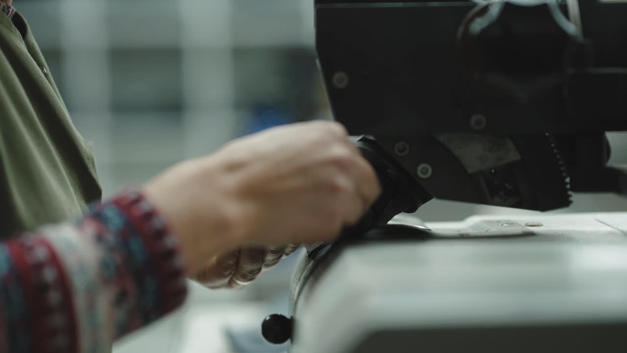 Worker guiding leather strap under industrial punching machine creating holes during footwear manufacturing process