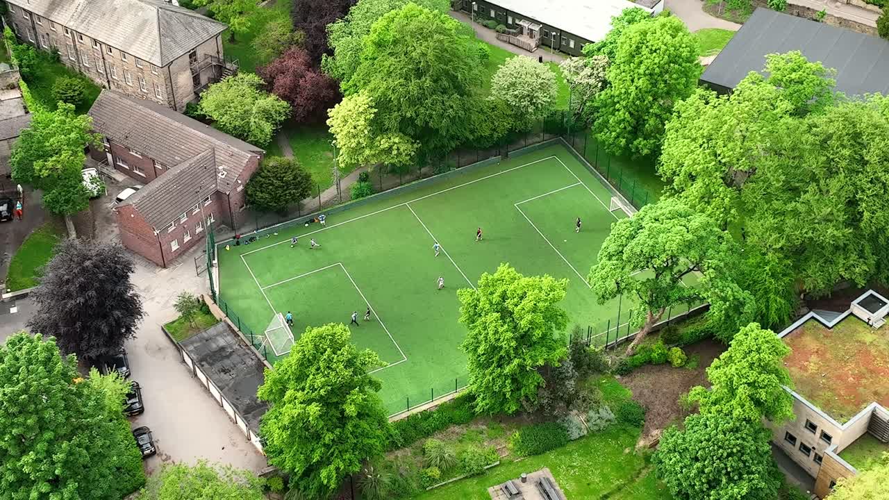 Two teams play soccer against each other on a green football pitch between the traditional residential houses in a luxury residential area in Sheffield