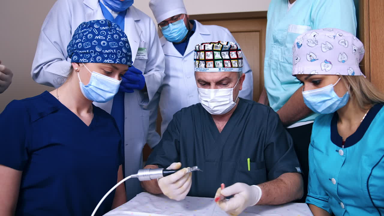 Adult male doctor showing the usage of drill machine. Attentive students look at teacher's work.