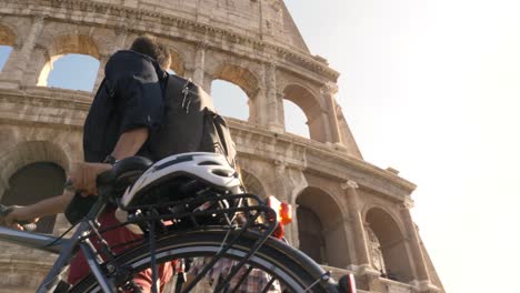 three young friends tourists walking with bikes and backpack at colosseum in rome on sunny day slow motion camera steadycam ground shot