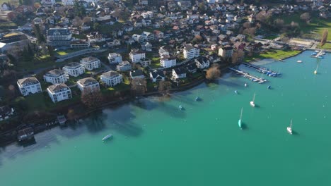 Ciudad-De-Spiez-Junto-Al-Lago-Thun-Con-Los-Alpes-Suizos-Como-Telón-De-Fondo,-Barcos-Tranquilos-Y-Aguas-Cristalinas,-Día-Soleado,-Vista-Aérea