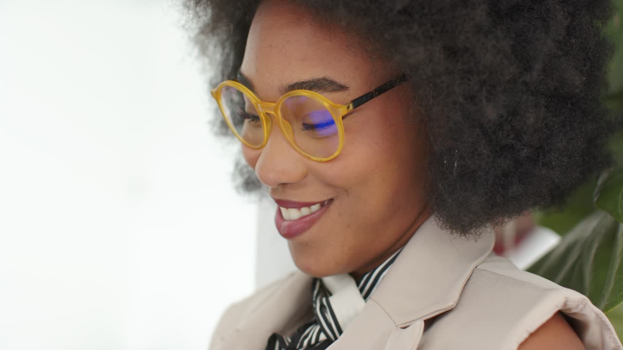 Femme afro-américaine recevant une notification, souriant puis tapotant une tablette, vêtue d'un blazer beige, au bureau