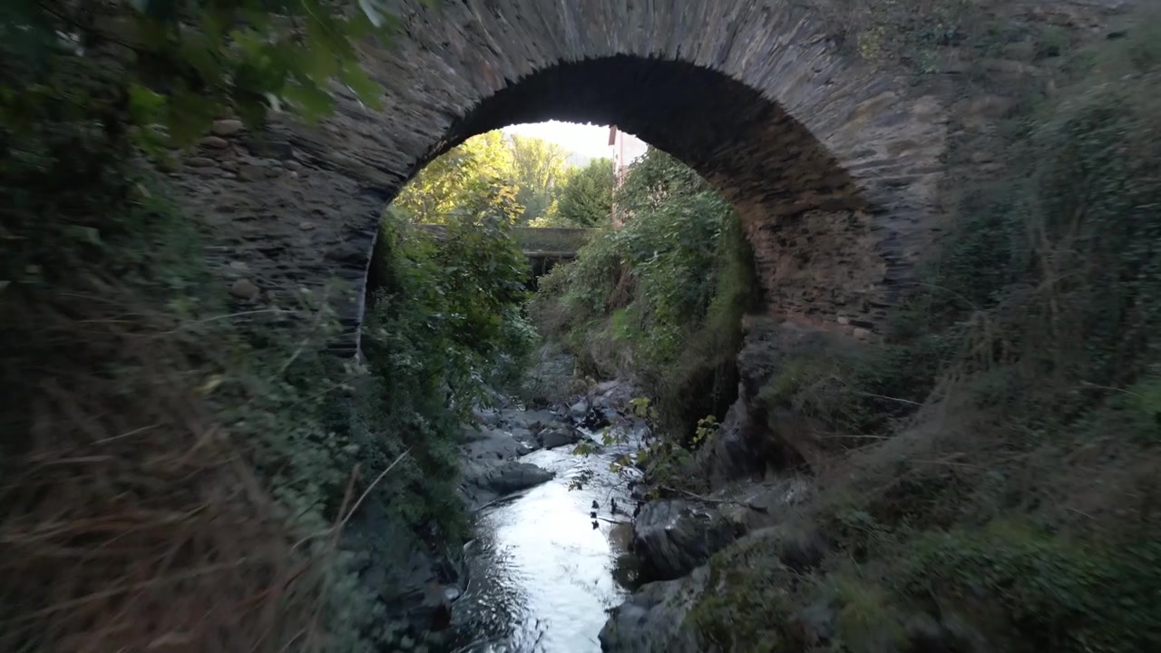Riacho rochoso serpenteia por vegetação densa perto da ponte romana em Éntoma, na Galiza, Espanha