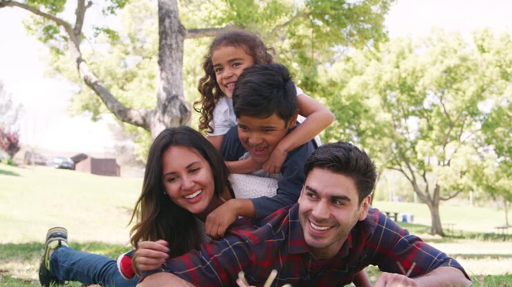 Young kids and parents lying in a pile on the grass in park