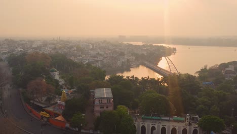 aerial view of a hazy city with a river and arch bridge at sunset