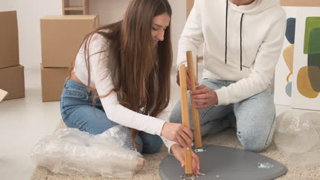 young couple moving into new house sitting on floor and assembling coffee table together 3