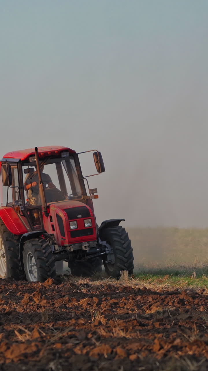 Red tractor at work. Agricultural machine plowing the field at daytime. Cultivation of land outdoors. Vertical video