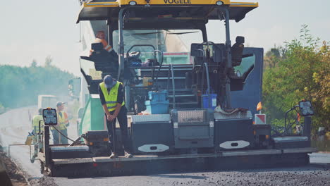 Process of lying new asphalt on the road. Group of workers in protective uniform working outdoors on the background of a big asphalt machinery.