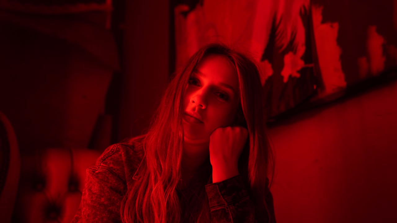 Female with long hair sitting in a bar with red neon lighting looking at the camera