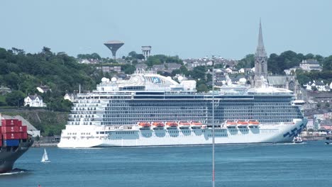 Heavy-traffic-in-Cork-harbour,-town-of-Cobh-with-moored-cruise-ship,-passing-small-boat,-sailboat,-and-cargo-ship