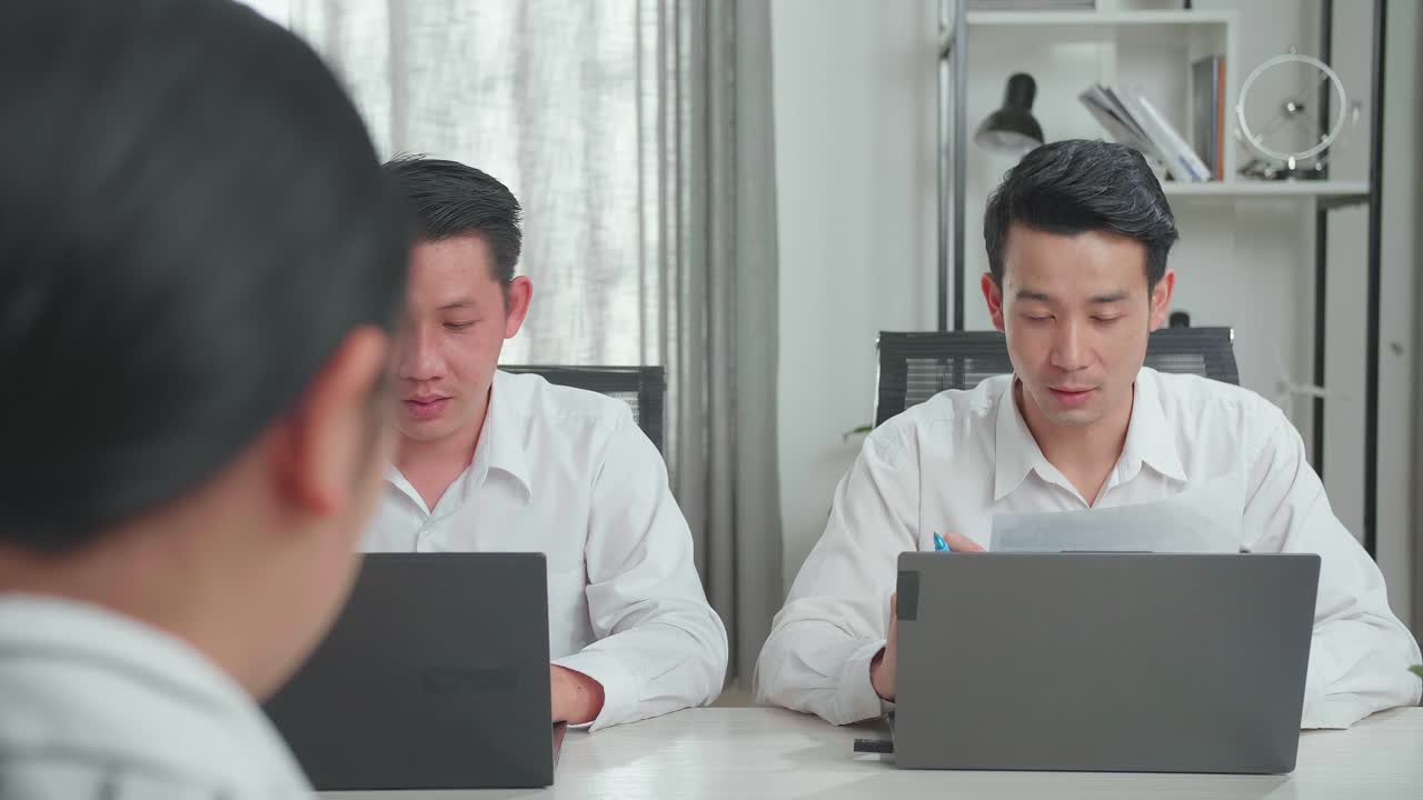 An Asian Businessman Holding A Paper And Talking To A Woman Interviewee While A Man Beside Him Is Typing During Interviewing At The Office