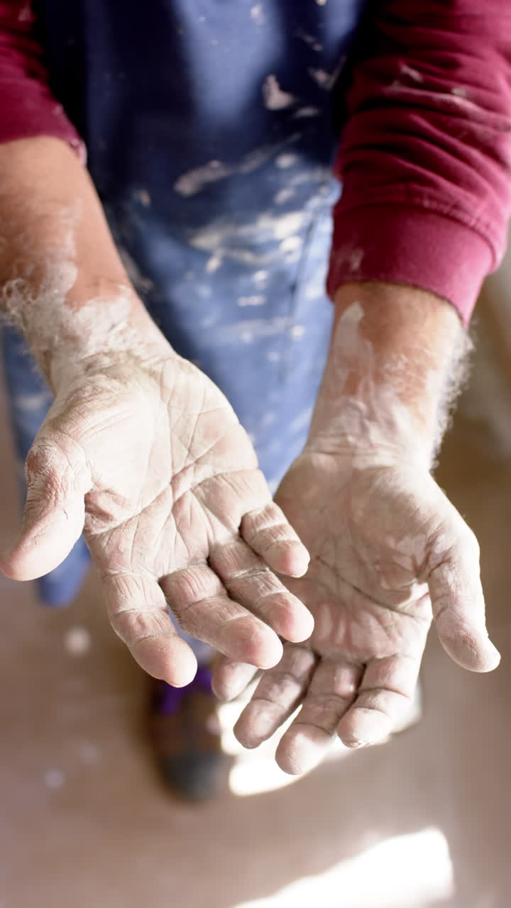 Dirty hands of biracial male potter with long beard, standing in pottery studio, slow motion