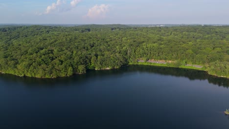 calm and deep blue water of kensico reservoir, vast green forest and scenic road surround lake, westchester county, new york, usa. aerial drone lateral view